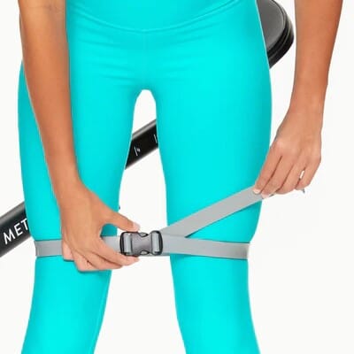 Woman adjusting The DB Method DreamBand Pro resistance strap while wearing aqua leggings.