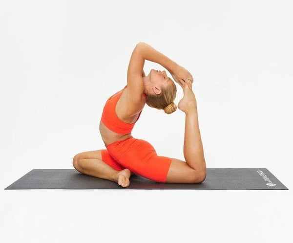 A woman in bright orange activewear, performing yoga on The DB Method gym mat.
