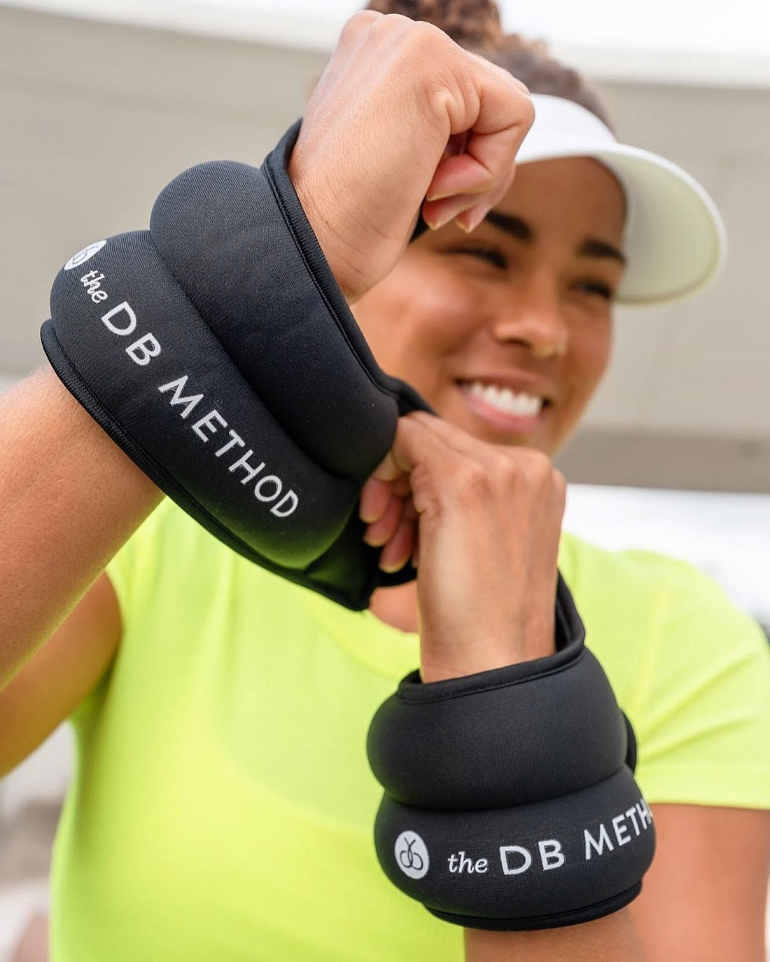 Woman smiling in workout gear while wearing The Dreamlets by The DB Method on both wrists.