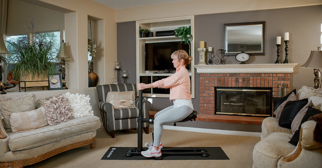 Woman using The DB Method machine for a seated squat workout in a cozy living room.