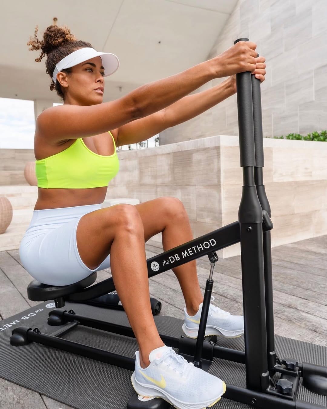 Woman in neon green top performing a squat on The DB Method Machine on a patio mat.