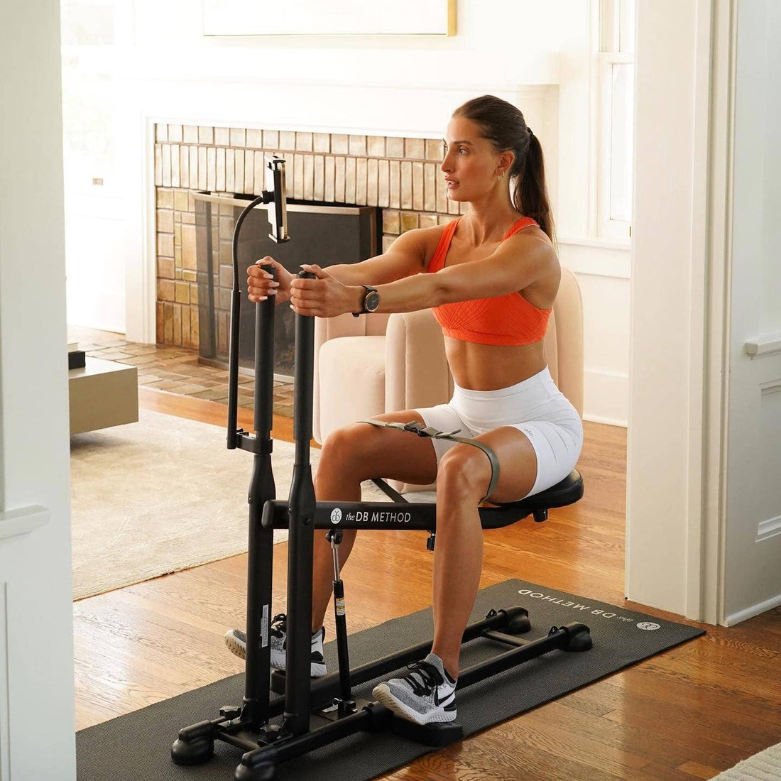 Woman exercises on The DB Method machine in a living room, gripping handles.
