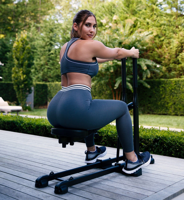 Woman in gray workout set using The DB Method squat machine on an outdoor deck.