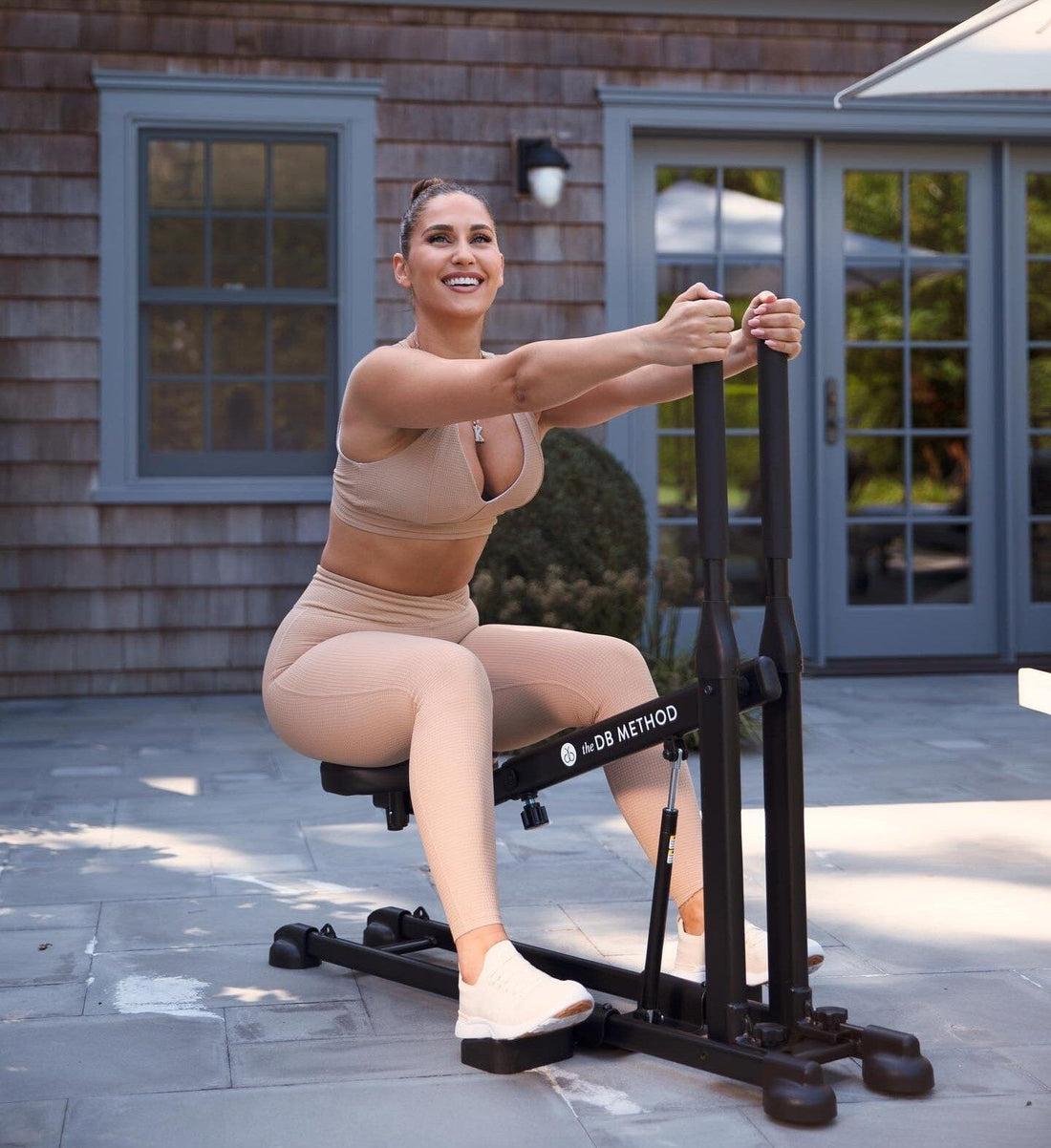A smiling woman uses The DB Method Squat Machine for an outdoor lower-body workout.