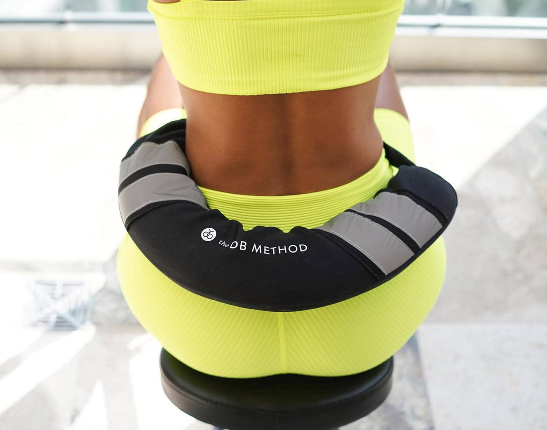 Woman in neon activewear wearing The DB Method DreamBelt during a seated glute workout.