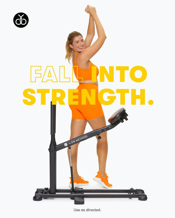 An enthusiastic woman in orange athletic wear raises her arms in front of The DB Method workout machine.