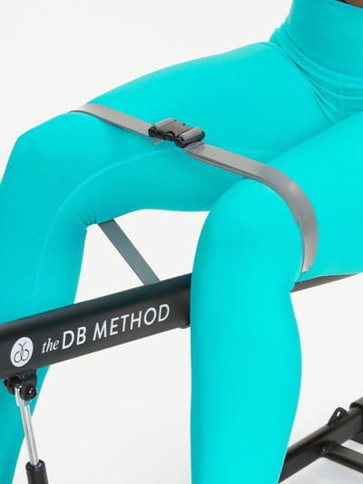 Close-up of a person wearing turquoise leggings using The DB Method machine with a resistance band.